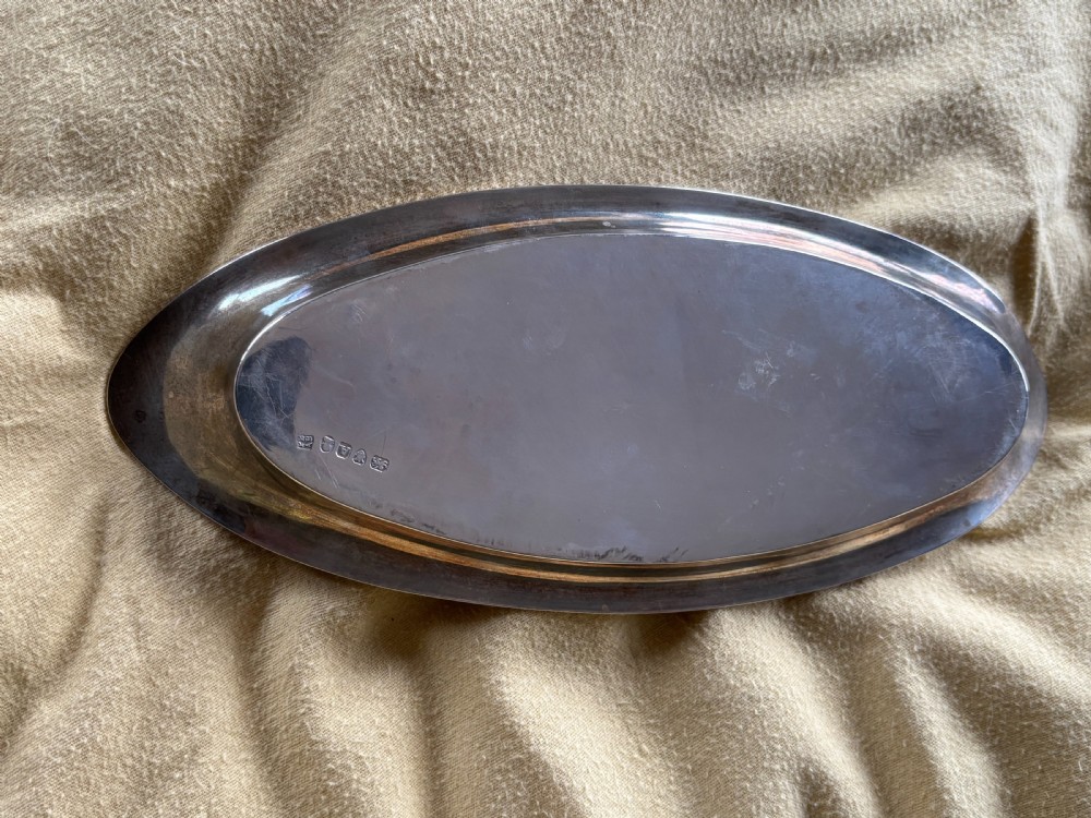 A George III sterling silver oval tray displaying visible British hallmarks stamped on its smooth inner rim.