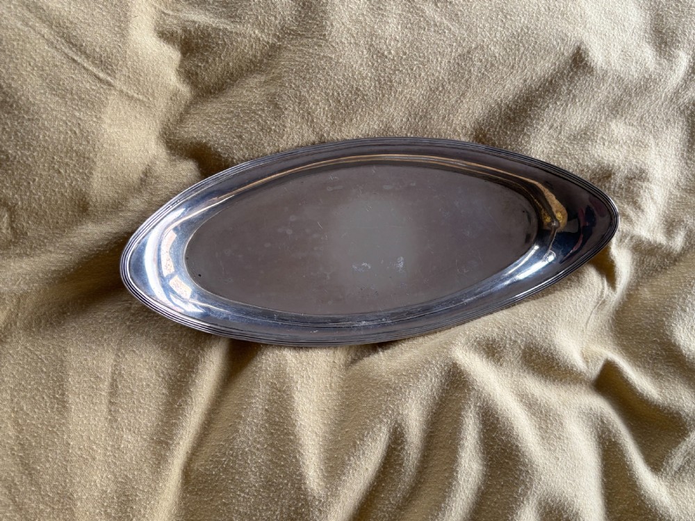 A George III sterling silver oval tray displaying visible British hallmarks stamped on its smooth inner rim. View II