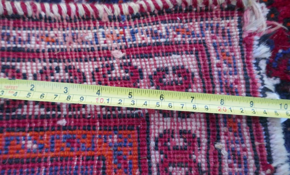 A rectangular hand-woven Persian wool carpet featuring a red stepped diamond centre, indigo blue spandrels, and geometric tribal borders. View IV