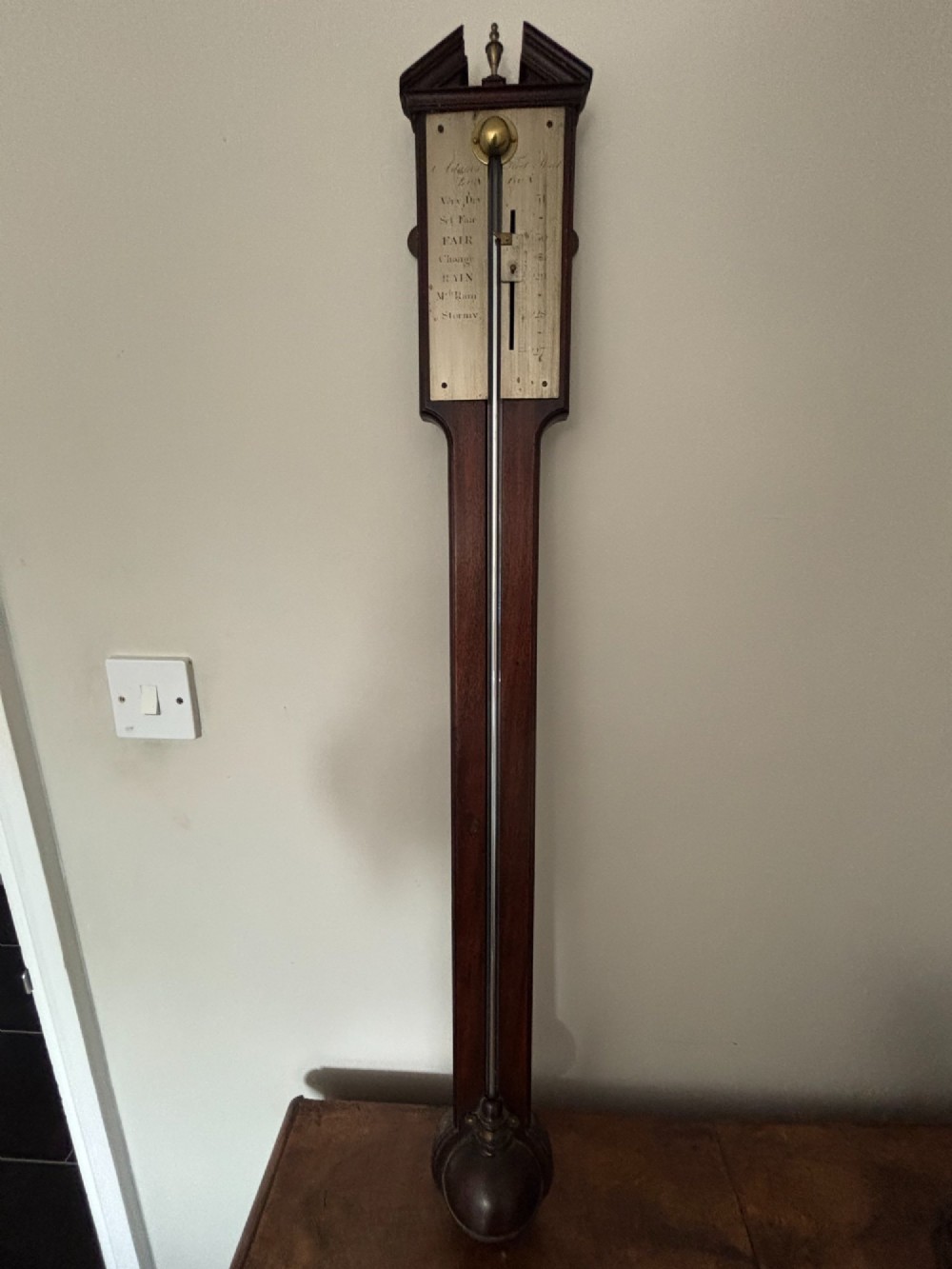 A late 18th-century Georgian mahogany stick barometer featuring a broken pediment top with a brass finial and an engraved silvered brass dial plate.