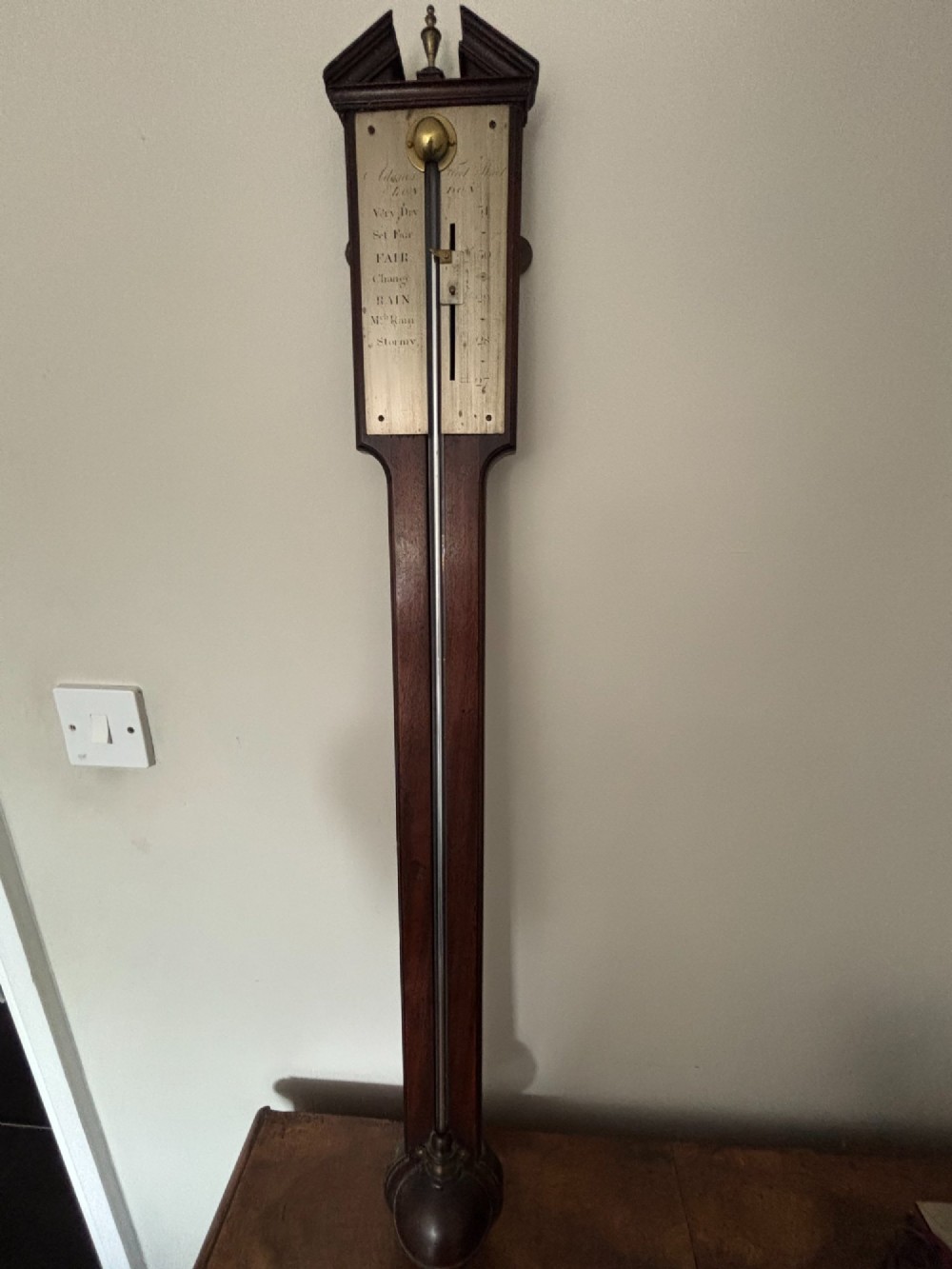 A late 18th-century Georgian mahogany stick barometer featuring a broken pediment top with a brass finial and an engraved silvered brass dial plate. View V