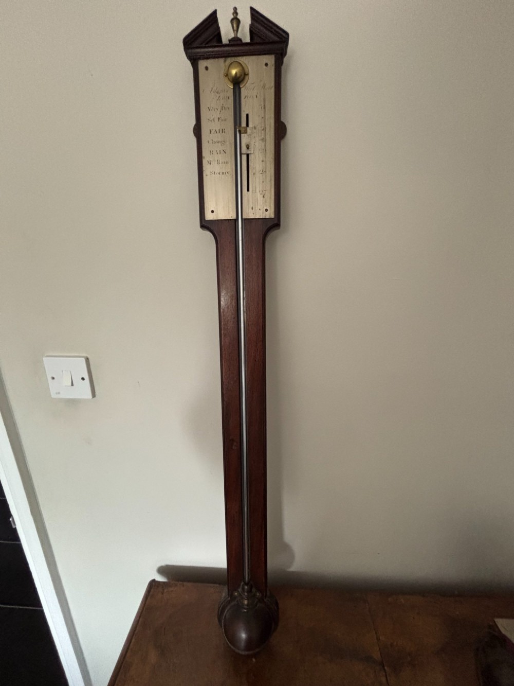 A late 18th-century Georgian mahogany stick barometer featuring a broken pediment top with a brass finial and an engraved silvered brass dial plate. View VI