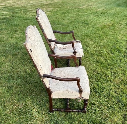 A pair of early 18th-century French walnut open armchairs with turned stretchers and worn floral tapestry upholstery. View V