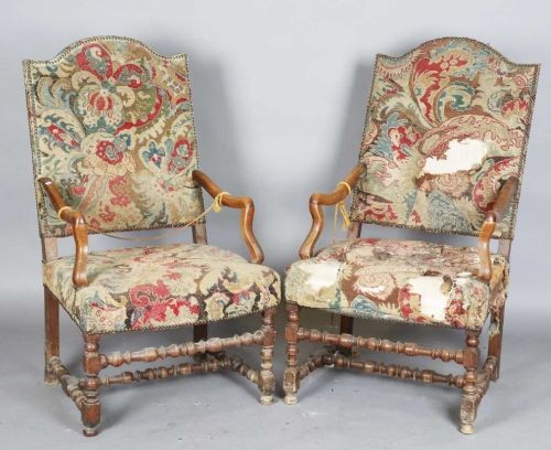 A pair of early 18th-century French walnut open armchairs with turned stretchers and worn floral tapestry upholstery.
