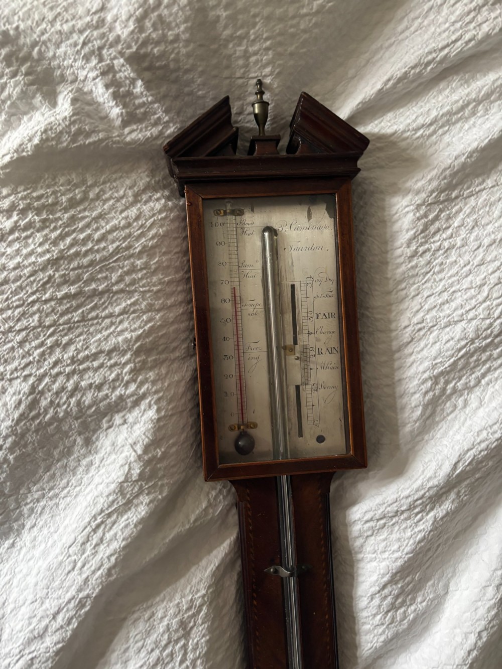 A Regency mahogany stick barometer featuring a pediment top, central mercury tube, thermometer, and an engraved silvered brass scale signed P. Caminada Taunton. View IV