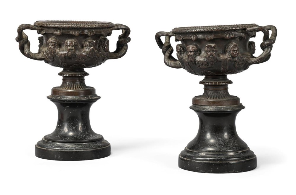 A pair of nineteenth-century patinated bronze Warwick vases with classical relief masks and woven handles, resting on black marble socles.