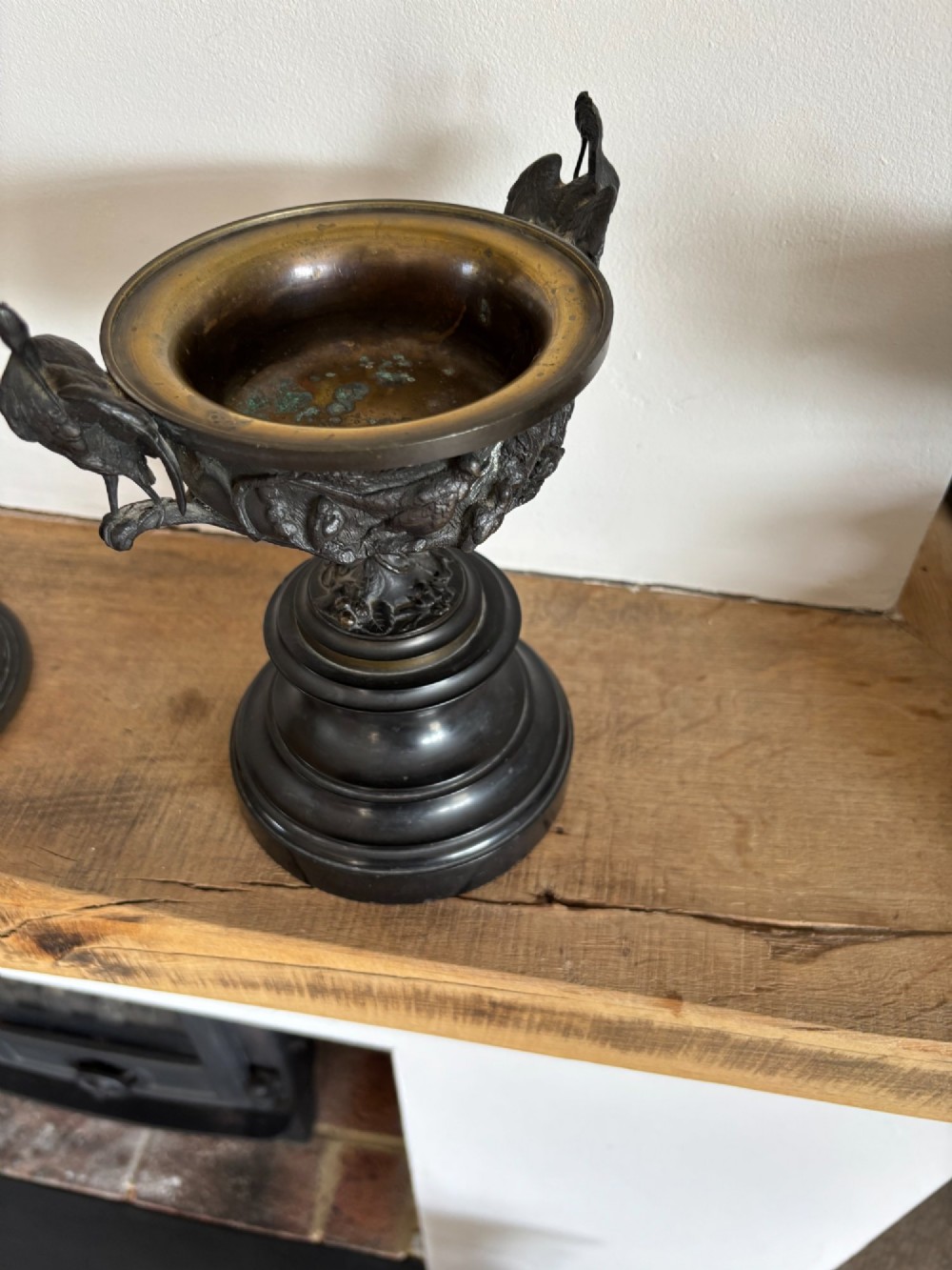 A pair of dark patinated bronze covered urns featuring relief-sculpted avian motifs and stork-shaped handles and finials on tiered bases. View VI