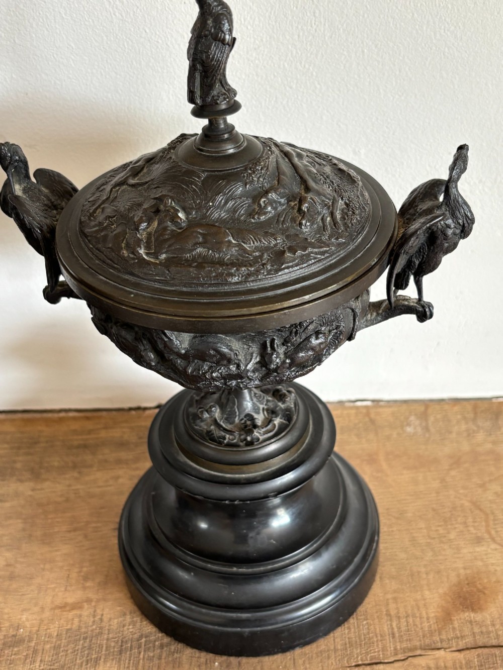A pair of dark patinated bronze covered urns featuring relief-sculpted avian motifs and stork-shaped handles and finials on tiered bases. View IX