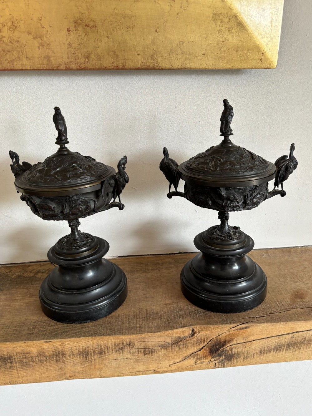 A pair of dark patinated bronze covered urns featuring relief-sculpted avian motifs and stork-shaped handles and finials on tiered bases. View XI