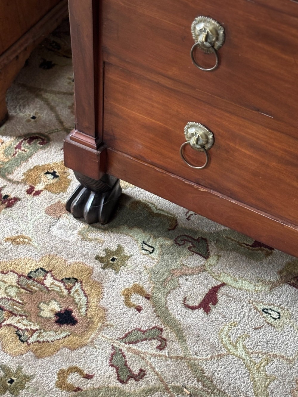An early nineteenth-century French Empire mahogany commode featuring three drawers with brass lion-mask ring handles, gilt female caryatid mounts at the upper corners, a dark veined marble top, and sculpted paw feet. View V