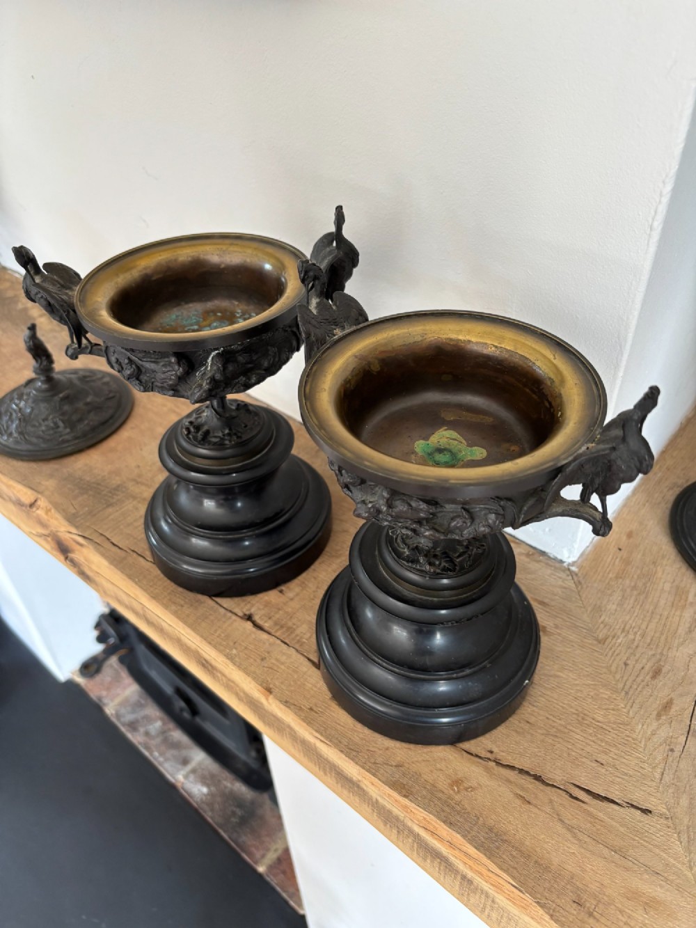 A pair of dark patinated bronze covered urns decorated with relief bird motifs and topped with stork finials on stepped pedestal bases. View VII