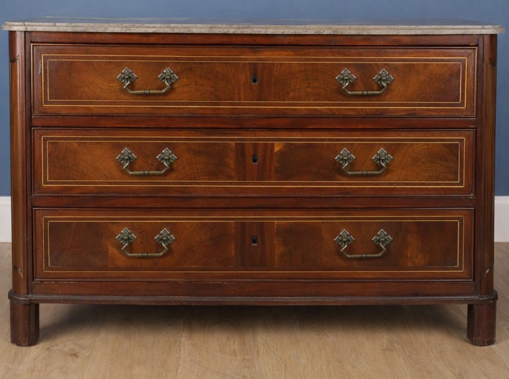 A late eighteenth-century French walnut and fruitwood commode featuring three drawers with string inlay, brass handles, and a grey marble top.