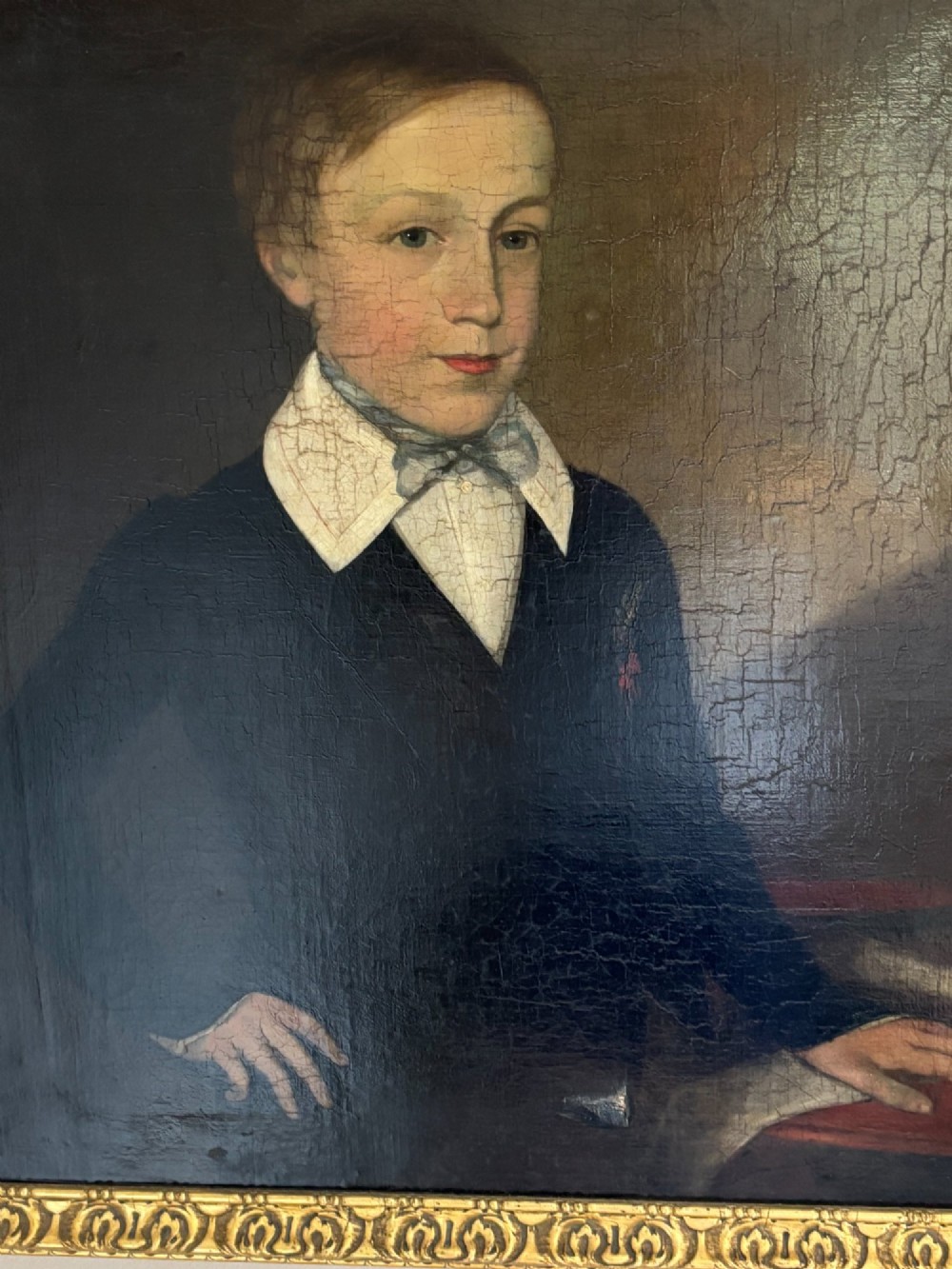 An antique oil portrait depicting a young male scholar in a dark blue coat and white collar, set in a gilded ornate frame. View V