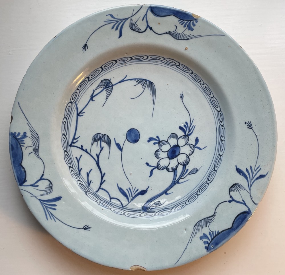 An 18th-century tin-glazed earthenware plate featuring hand-painted cobalt blue chinoiserie floral motifs on a pale blue-white ground.