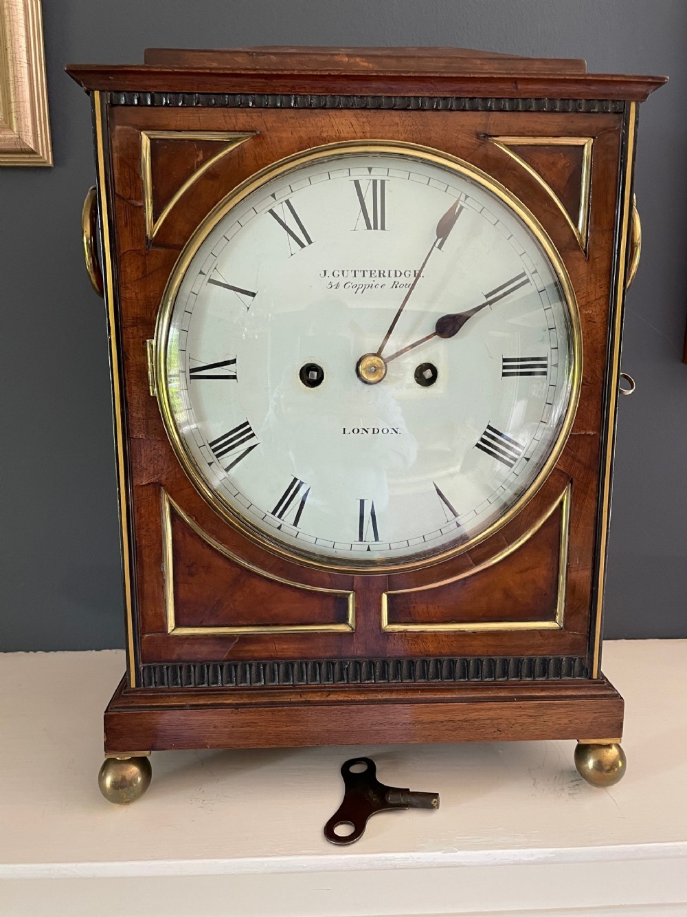 A Regency mahogany bracket clock featuring brass line inlay, ring side handles, brass ball feet, and a white circular dial with Roman numerals.
