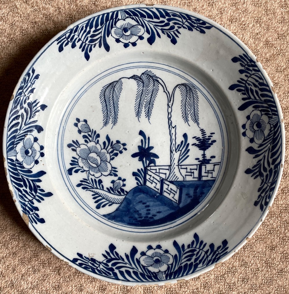 An eighteenth-century circular English delftware charger hand-painted with cobalt blue chinoiserie landscape motifs on a tin-glazed white surface.