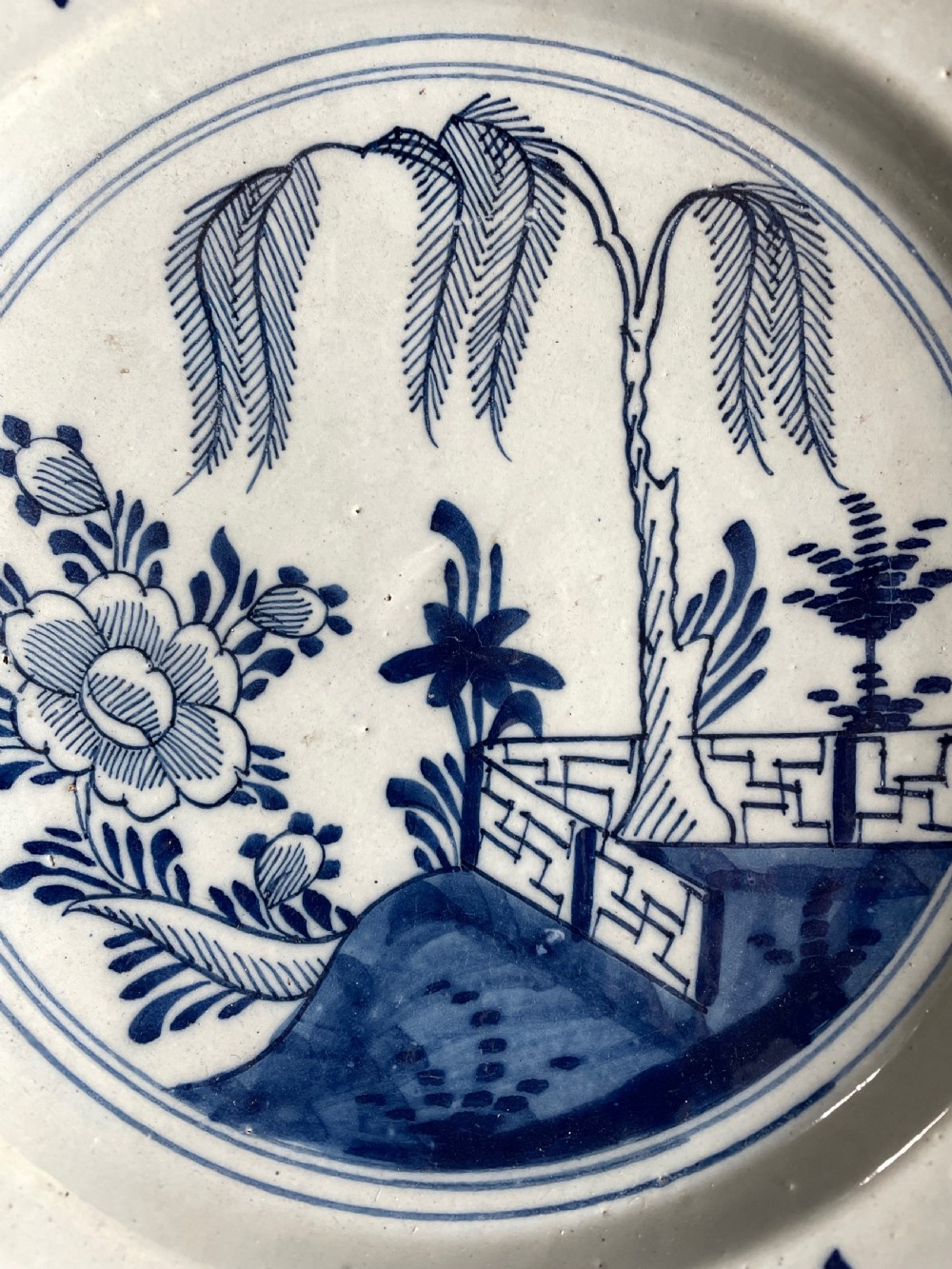 An eighteenth-century circular English delftware charger hand-painted with cobalt blue chinoiserie landscape motifs on a tin-glazed white surface. View II