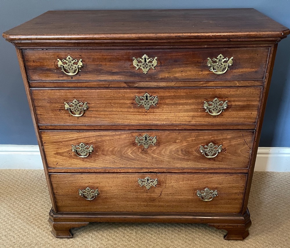 A small 19th-century wooden chest of drawers featuring four graduated drawers with pierced brass handles and bracket feet.