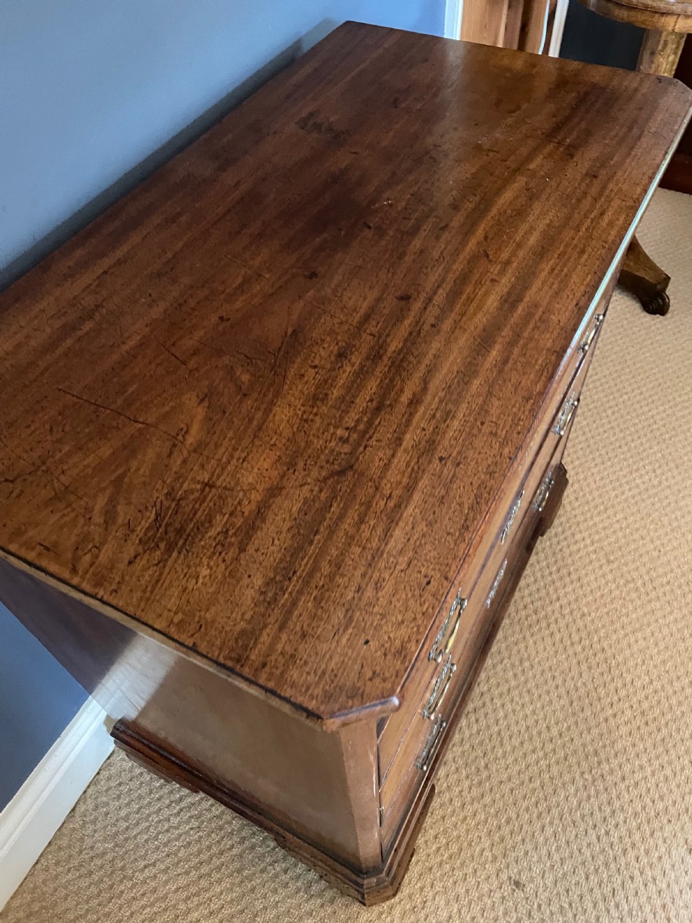 A small 19th-century wooden chest of drawers featuring four graduated drawers with pierced brass handles and bracket feet. View V