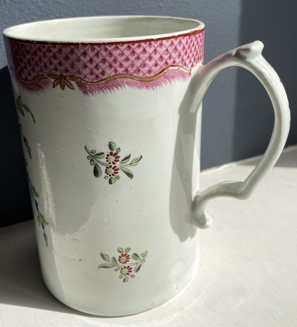 A cylindrical 18th-century soft-paste porcelain tankard featuring hand-painted polychrome florals, a central urn motif, and a pink diaper-pattern rim border. View IV