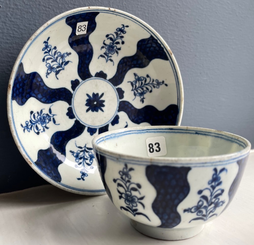 An 18th-century Lowestoft soft-paste porcelain tea bowl and saucer set decorated in underglaze cobalt blue with wavy bands and floral sprays.