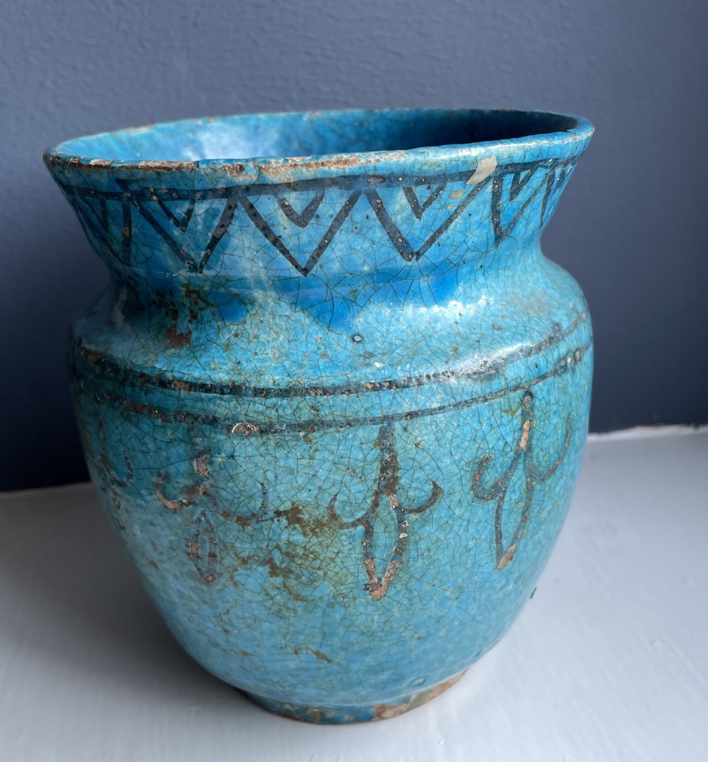 A turquoise glazed ceramic vessel with a flared rim, painted black geometric markings, and fine surface craquelure.