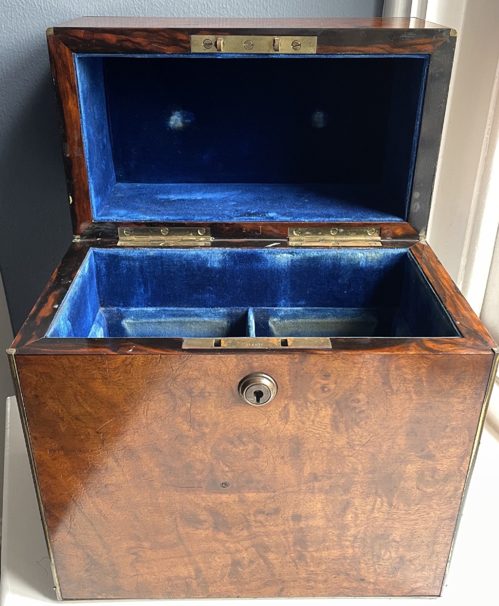 A closed rectangular burr walnut decanter box featuring thin brass trim around the outer edges and a circular brass keyhole escutcheon. View III