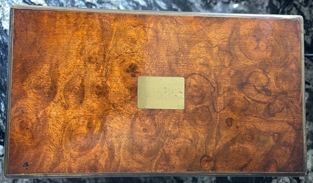 A closed rectangular burr walnut decanter box featuring thin brass trim around the outer edges and a circular brass keyhole escutcheon. View IV