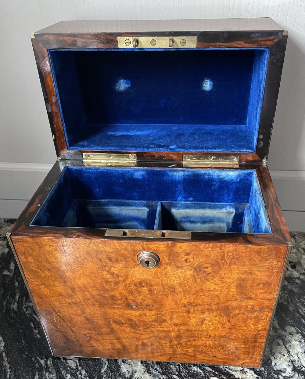 A closed rectangular burr walnut decanter box featuring thin brass trim around the outer edges and a circular brass keyhole escutcheon. View V