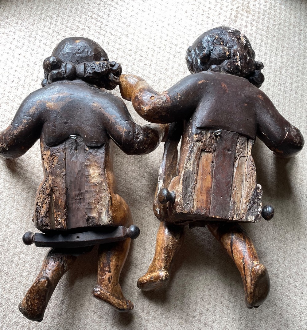 A pair of 17th-century French carved limewood putti featuring curly hair, draped sashes, and dynamic seated poses with a warm aged surface patina. View IV
