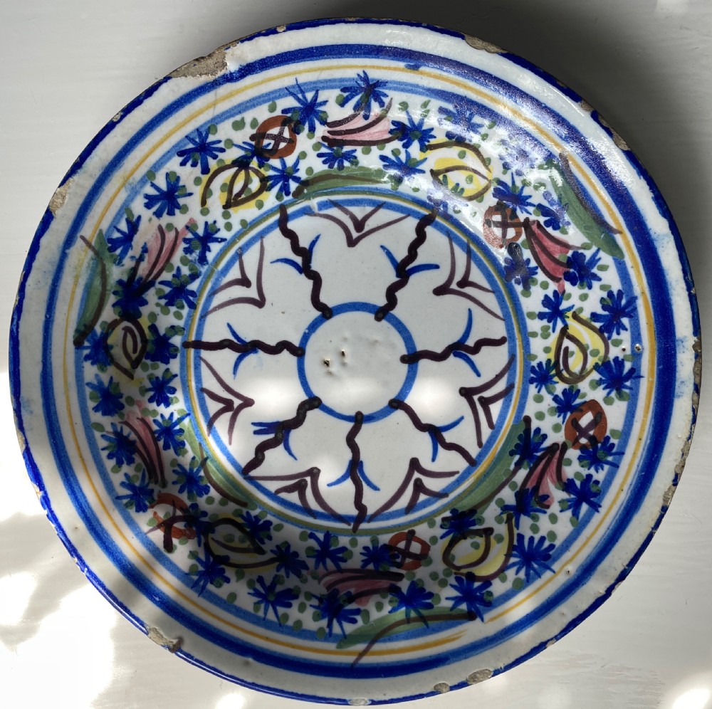 A circular nineteenth-century French tin-glazed earthenware bowl featuring hand-painted floral motifs and geometric borders in blue, green, yellow, and manganese hues on a white ground.