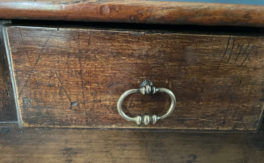 A nineteenth-century Chinese elm side table featuring three drawers with brass drop handles and straight legs set against a dark blue wall. View II
