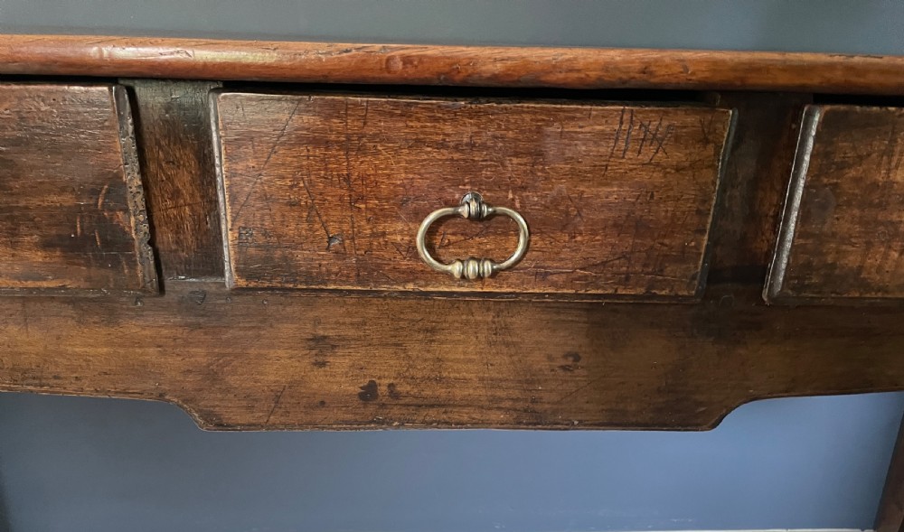 A nineteenth-century Chinese elm side table featuring three drawers with brass drop handles and straight legs set against a dark blue wall. View III
