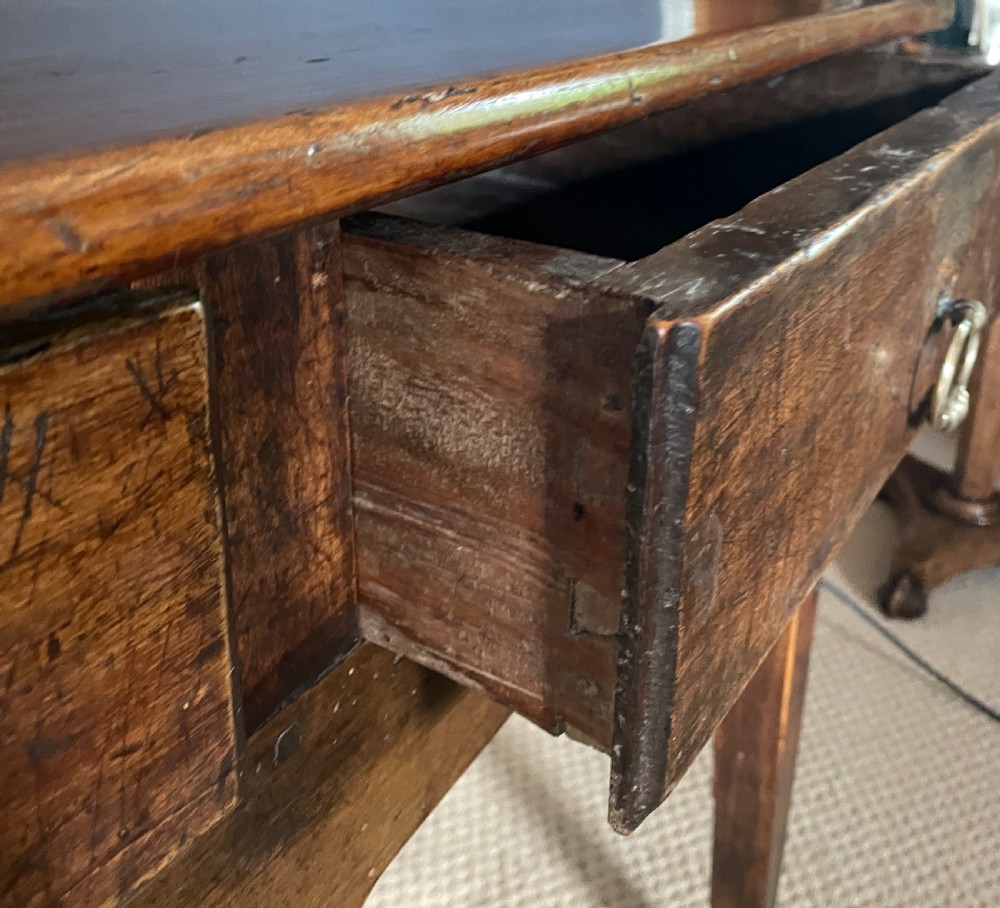 A nineteenth-century Chinese elm side table featuring three drawers with brass drop handles and straight legs set against a dark blue wall. View VI