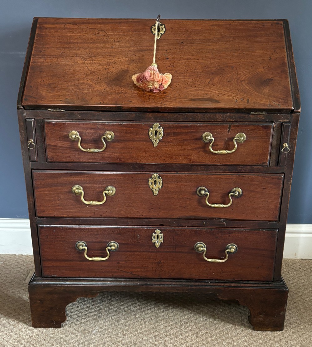 A small George III mahogany slant-front bureau featuring three drawers with brass swan-neck handles and bracket feet.