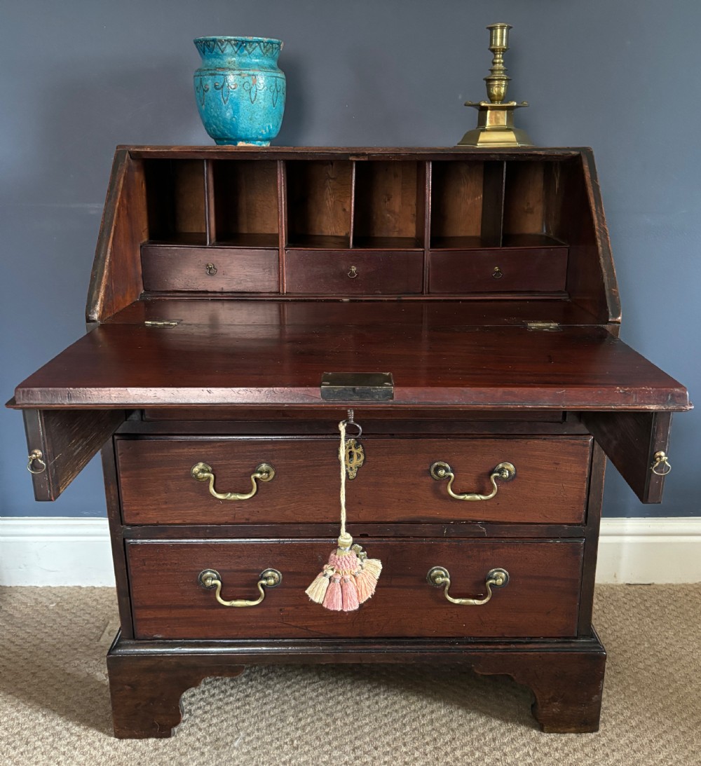 A small George III mahogany slant-front bureau featuring three drawers with brass swan-neck handles and bracket feet. View II