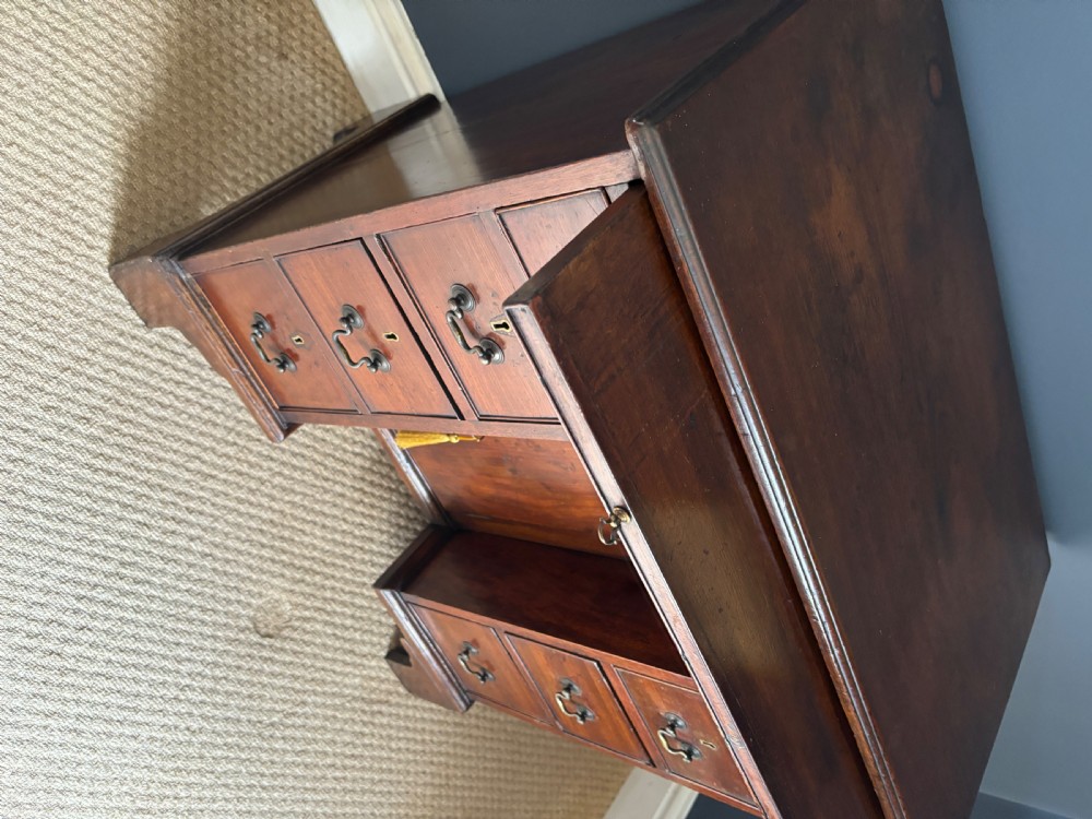 An antique Georgian Cuban mahogany kneehole desk featuring six small pedestal drawers flanking a central recessed arched cupboard door, a full-width top drawer, brass handles, and bracket feet. View II