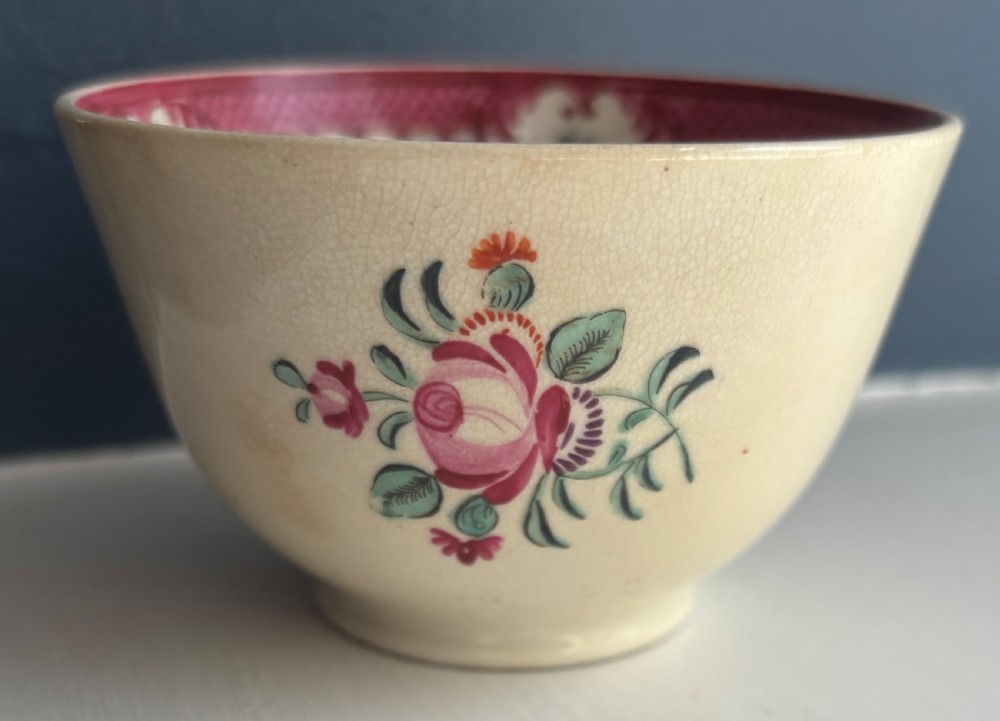 An 18th-century creamware tea bowl decorated with hand-painted floral motifs and an ornate pink interior border.