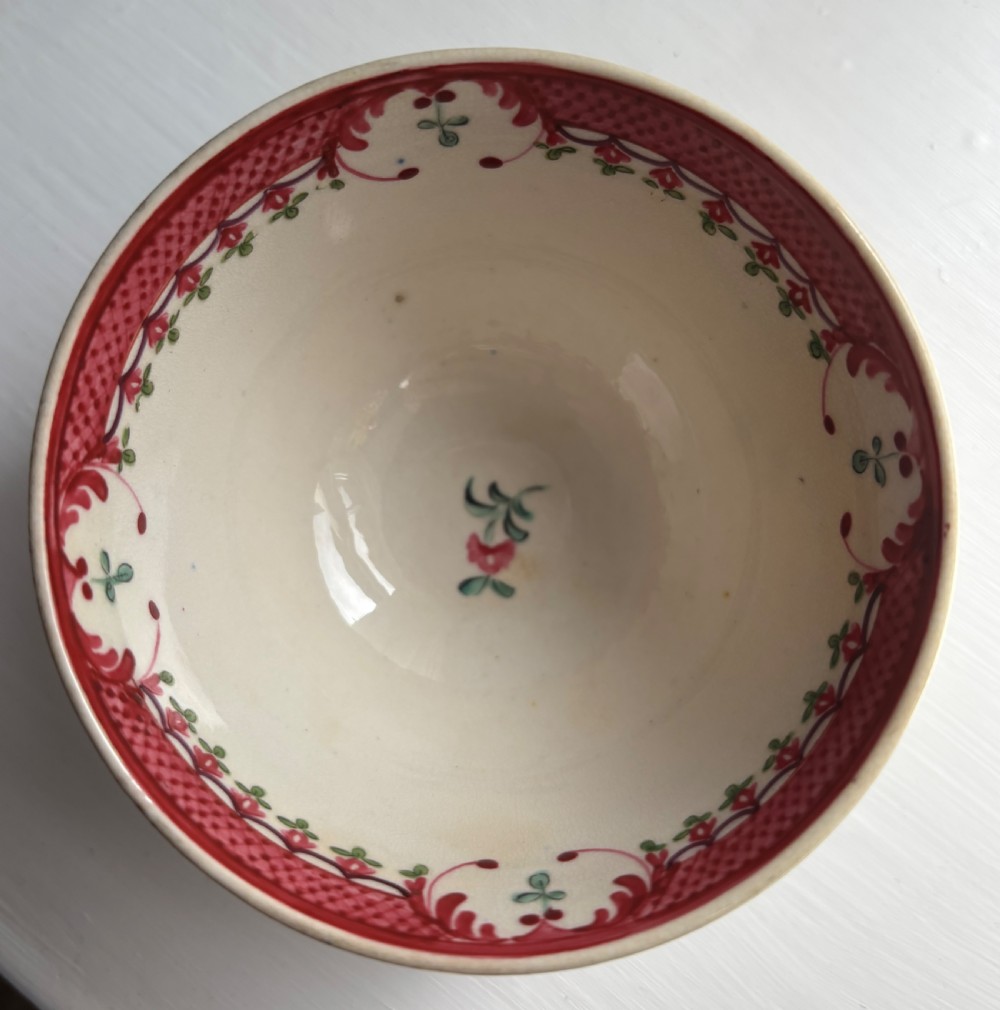 An 18th-century creamware tea bowl decorated with hand-painted floral motifs and an ornate pink interior border. View II