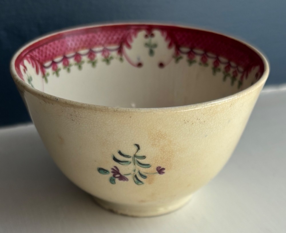 An 18th-century creamware tea bowl decorated with hand-painted floral motifs and an ornate pink interior border. View IV