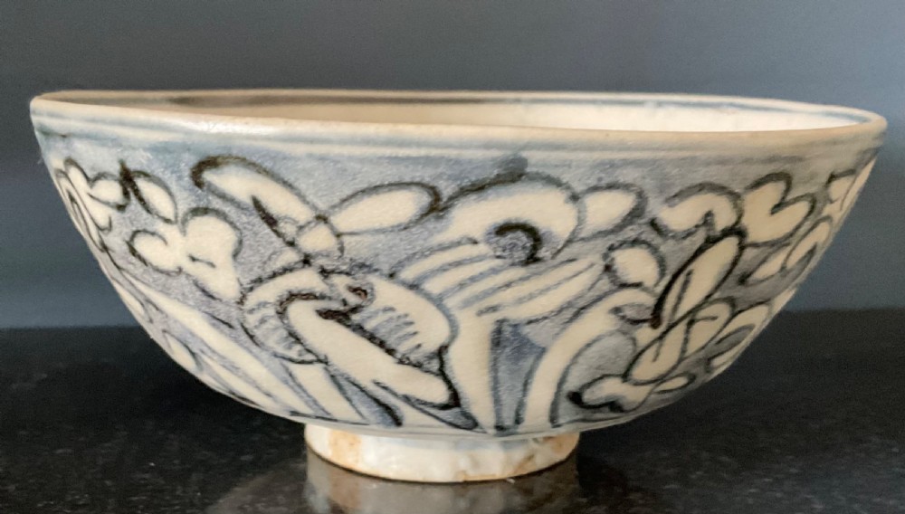 A circular blue and white ceramic bowl painted with underglaze cobalt floral motifs resting on an unglazed raised foot rim.
