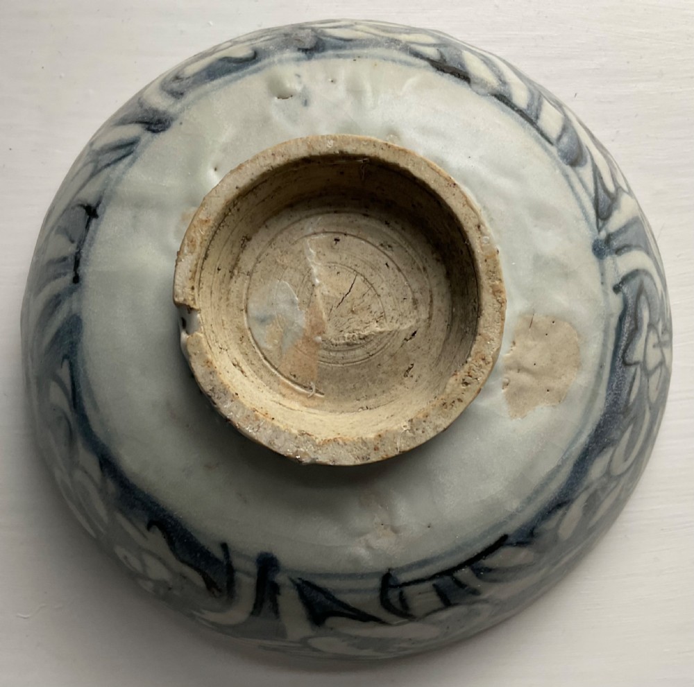 A circular blue and white ceramic bowl painted with underglaze cobalt floral motifs resting on an unglazed raised foot rim. View II
