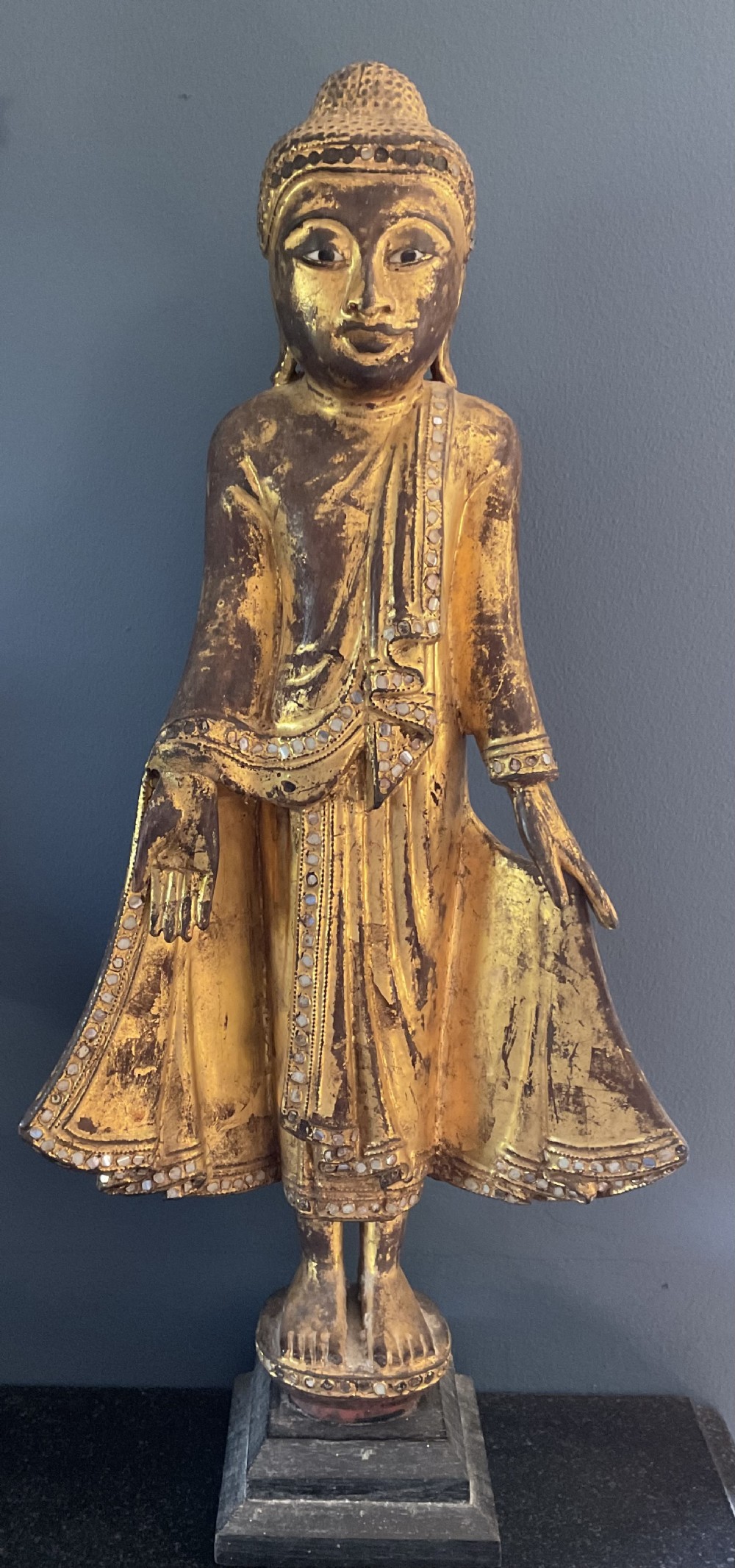 An early twentieth-century Burmese Mandalay standing Buddha figure rendered in carved wood with a gold leaf finish and glass mosaic border details.