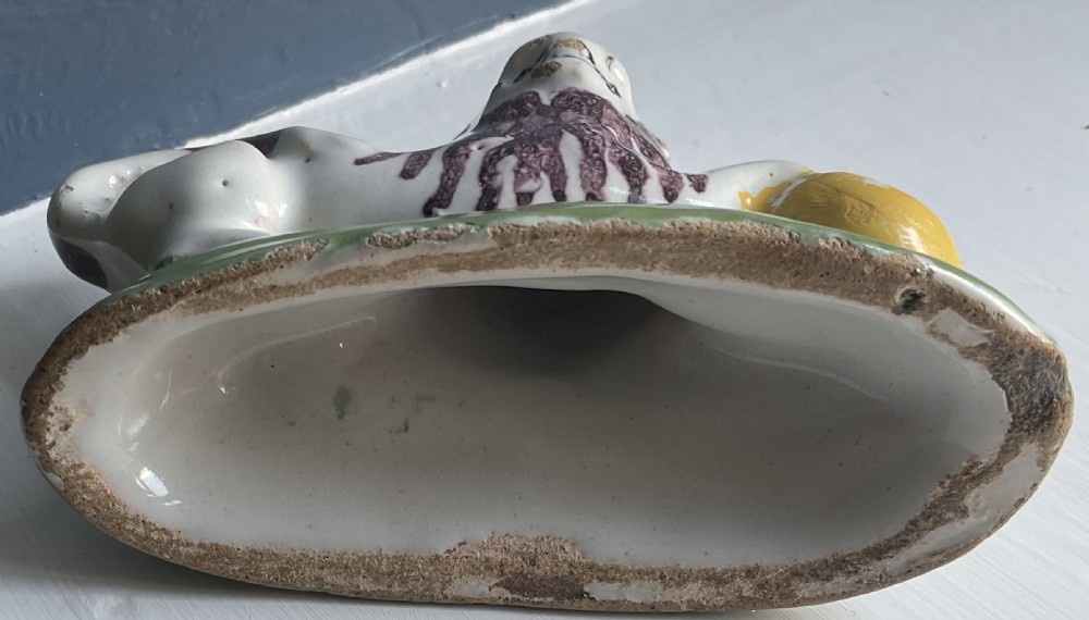 A tin-glazed ceramic figure of a reclining lion resting its paw on a yellow ball, featuring manganese brush-painted accents and a green base. View II
