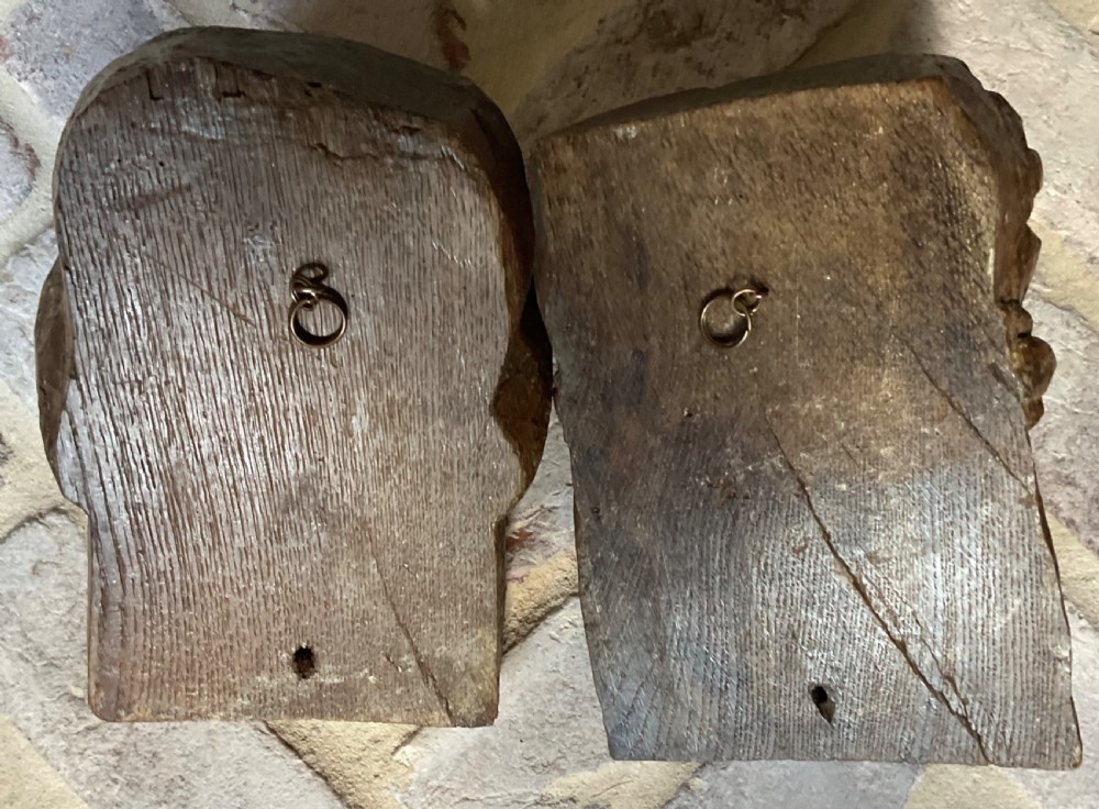 A pair of 17th-century carved oak corbels featuring detailed human heads with distinct facial expressions and headdresses. View V