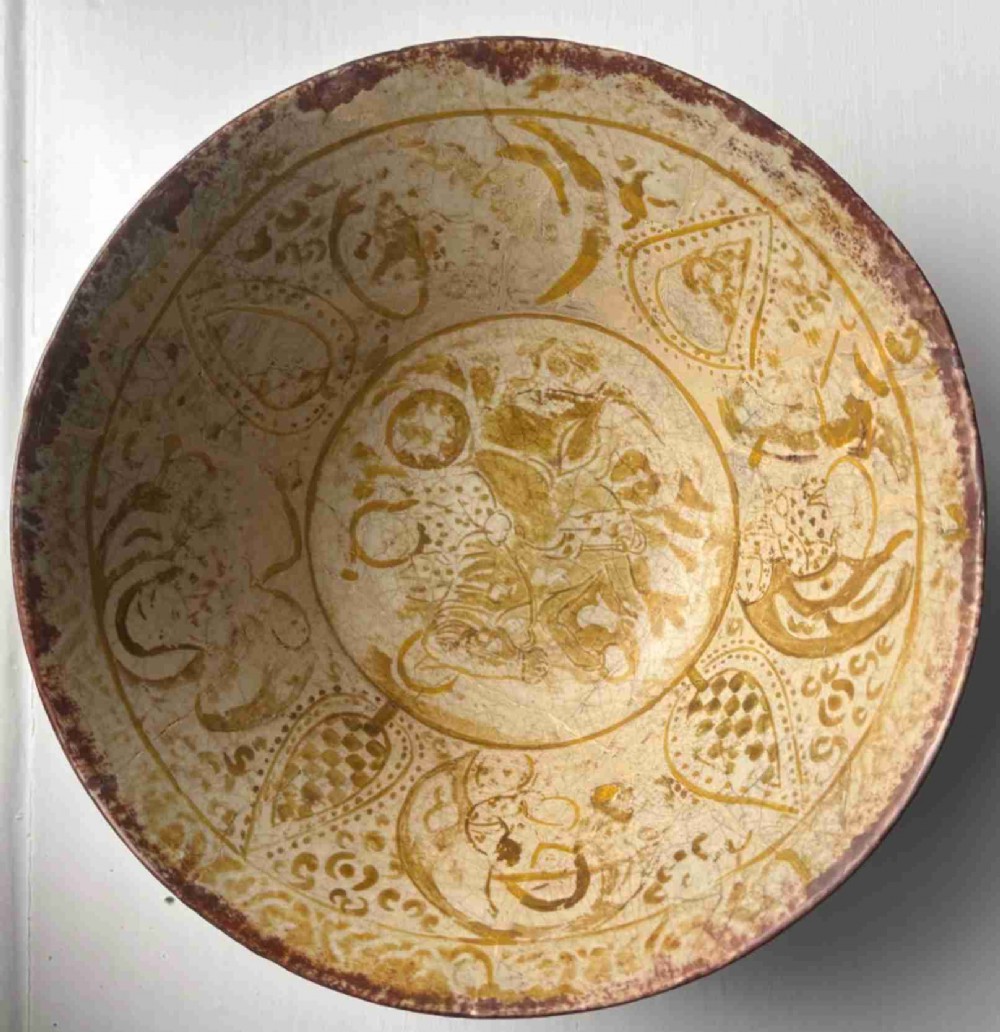 A round antique Persian ceramic footed bowl featuring golden-ochre lustre painted motifs and geometric borders on a craquelure off-white glaze.