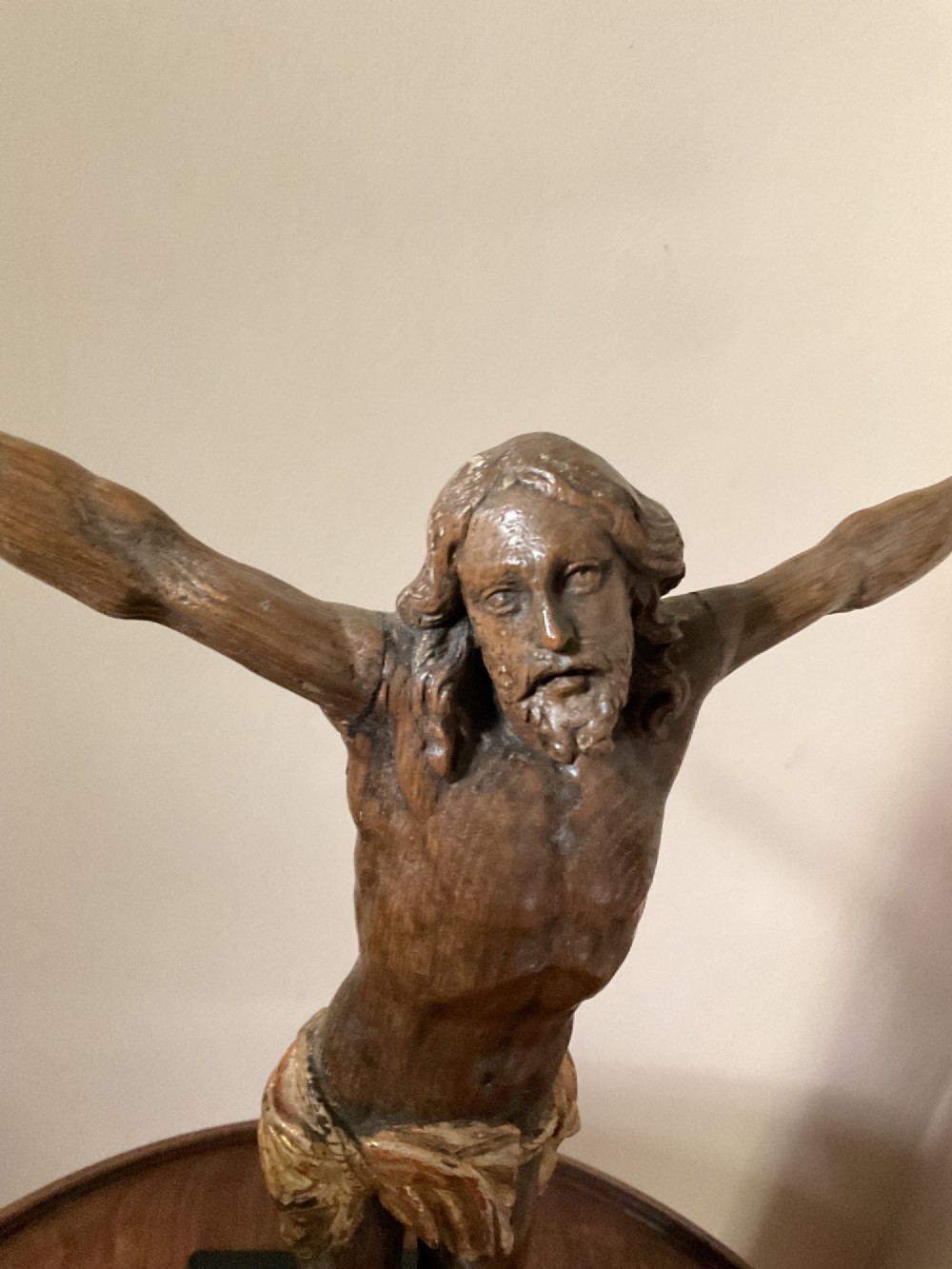 A carved wooden 17th-century Corpus Christi figure with outstretched arms and a gilded perizoma, mounted vertically on a black square metal display stand. View II