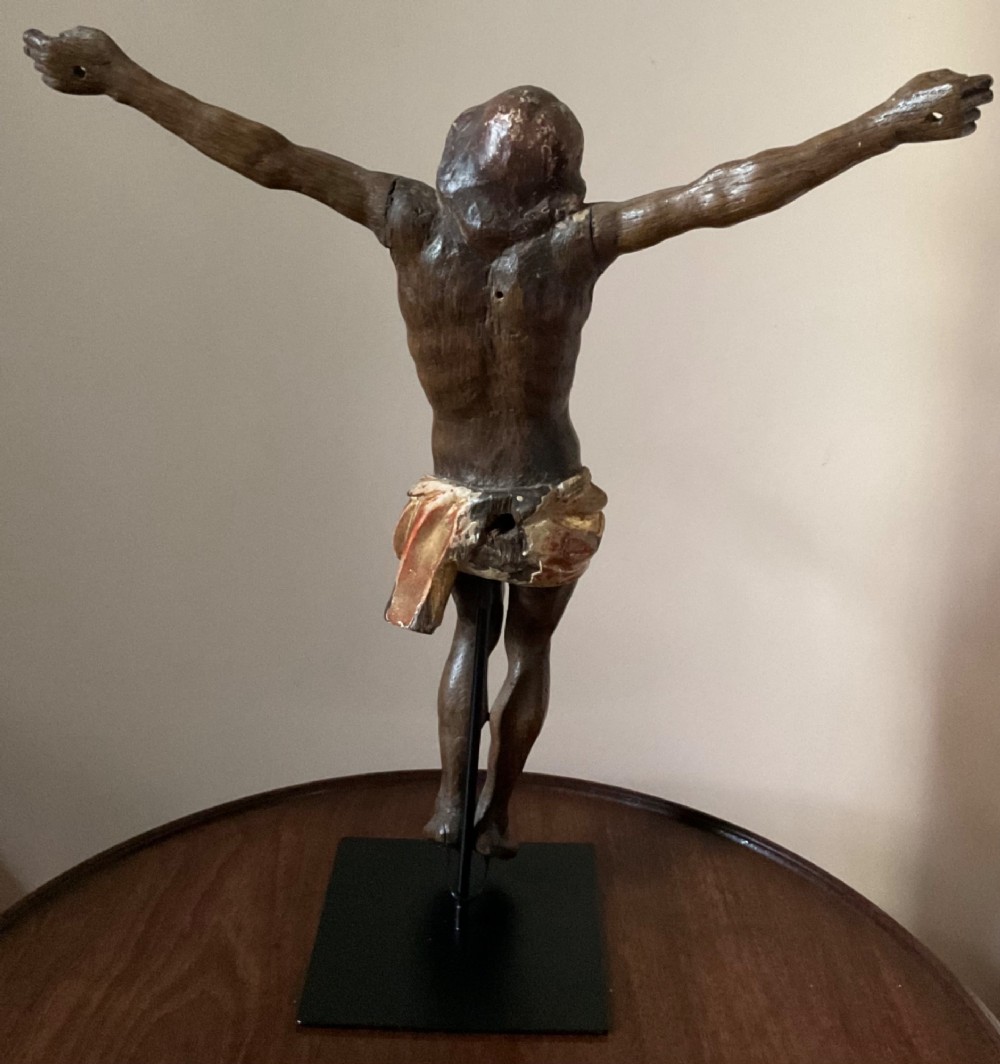 A carved wooden 17th-century Corpus Christi figure with outstretched arms and a gilded perizoma, mounted vertically on a black square metal display stand. View III