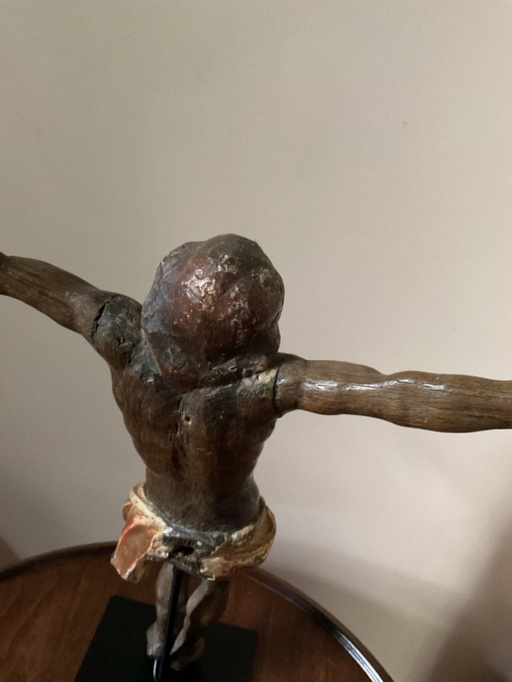 A carved wooden 17th-century Corpus Christi figure with outstretched arms and a gilded perizoma, mounted vertically on a black square metal display stand. View IV