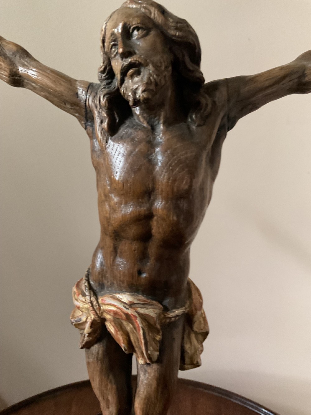 A carved wooden 17th-century Corpus Christi figure with outstretched arms and a gilded perizoma, mounted vertically on a black square metal display stand. View V